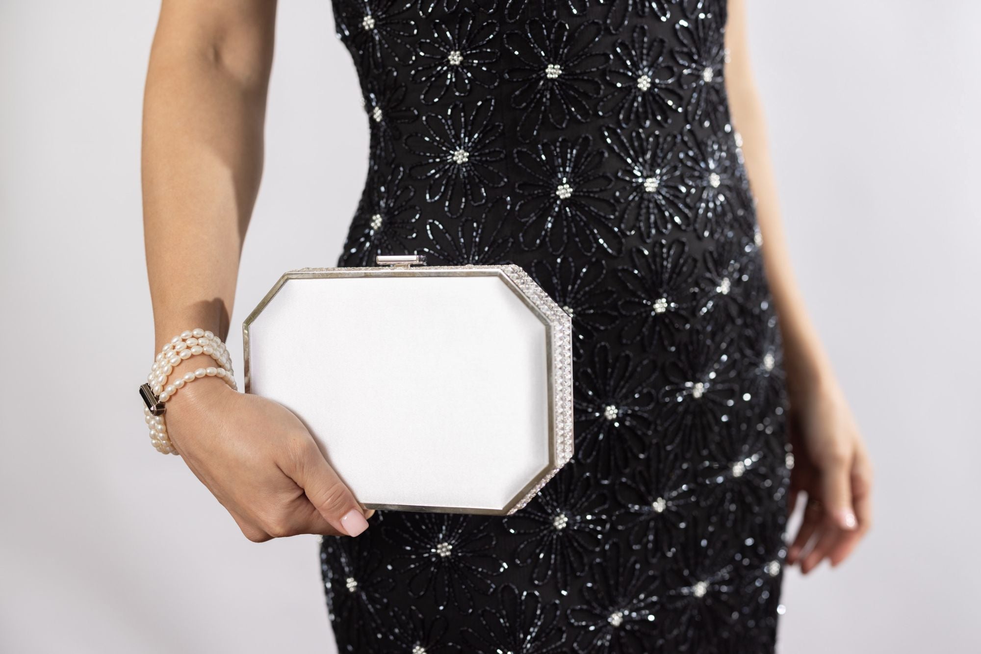 Woman wearing black evening cocktail dress holding white satin Como Clutch.