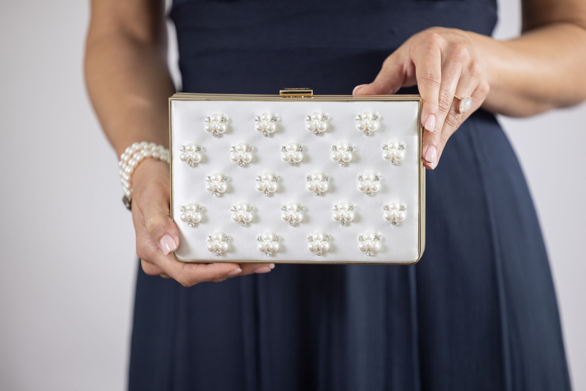 Woman wearing black dress holds white satin Venezia Clutch with pear and crystal beading.