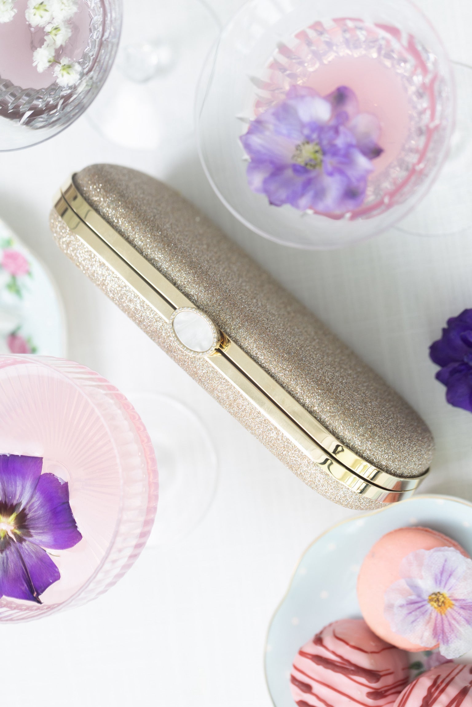 A gold clutch, flowers, and desserts on a table.
