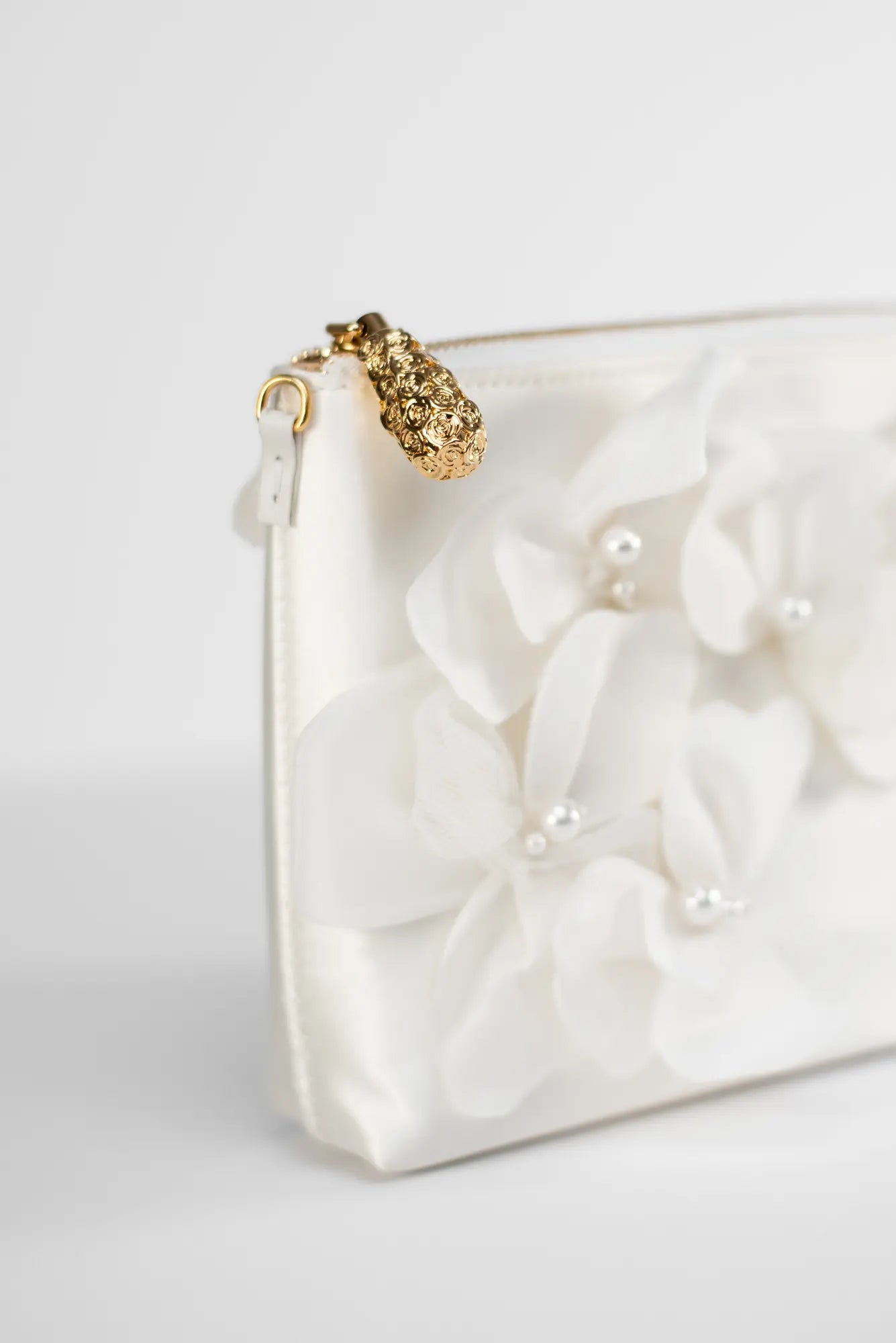 Close-up of the Hayden Clutch Purse from The Bella Rosa Collection, made with ivory duchess satin and adorned with organza floral designs and pearls, featuring a gold-toned zipper pull - available in the Sample Sale.