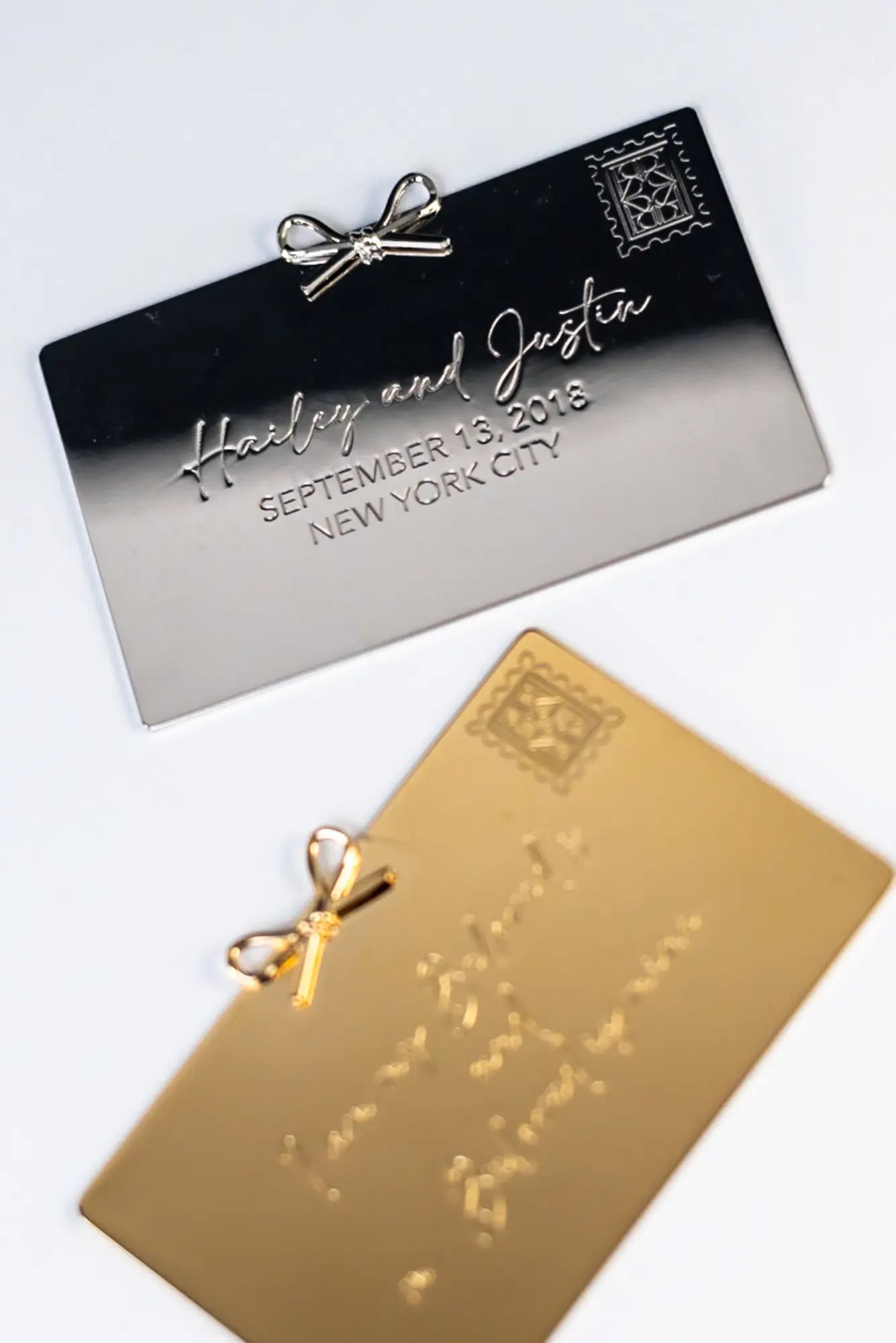 Two elegant metallic cards from The Bella Rosa Collection feature embossed text and a delicate bow design. The silver card reads "Hailey and Justin, September 13, 2018, New York City," while the gold card mirrors this style. Perfect as a Personalized Plaque Sentiment Engraving.