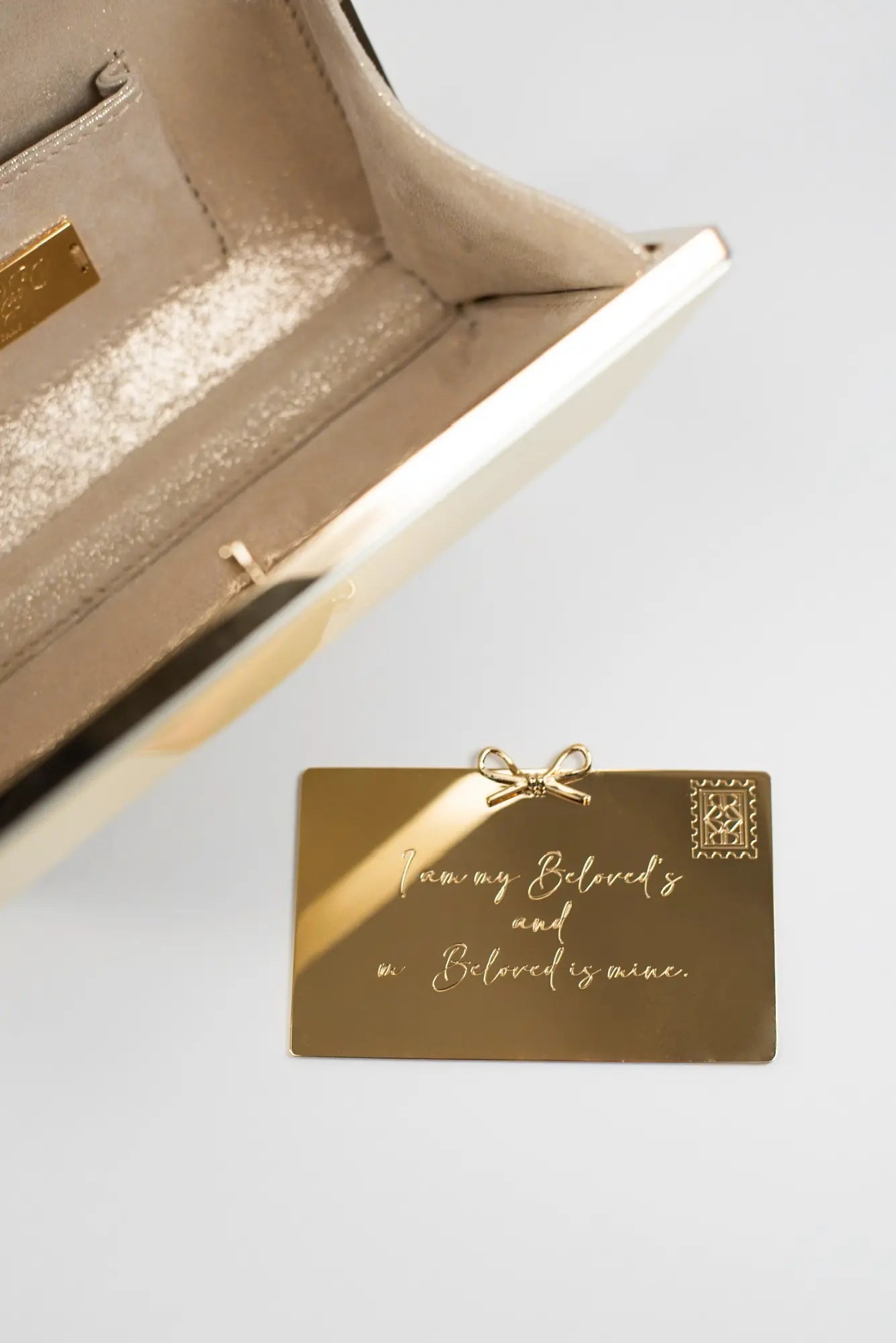 A gold credit card featuring the Personalized Plaque Sentiment Engraving lies on a surface near an open beige bag from The Bella Rosa Collection.