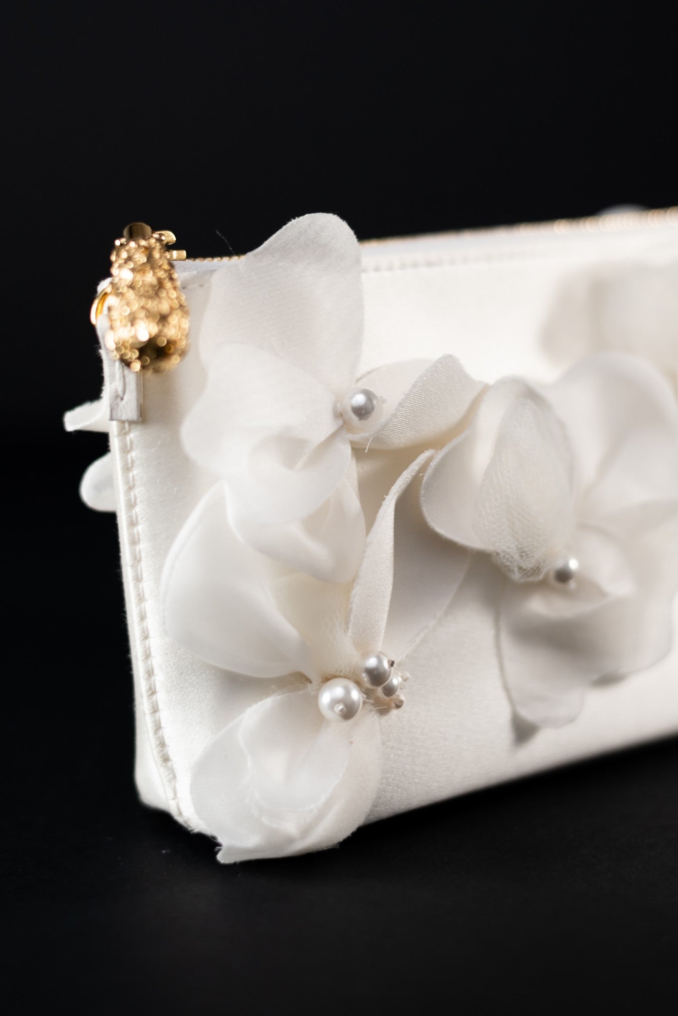 The Hayden Clutch Purse Organza Flowers from The Bella Rosa Collection, featuring an ivory duchess satin finish with delicate fabric flowers and pearl embellishments, and a gold clasp, set against a black background, highlights exquisite Italian craftsmanship.