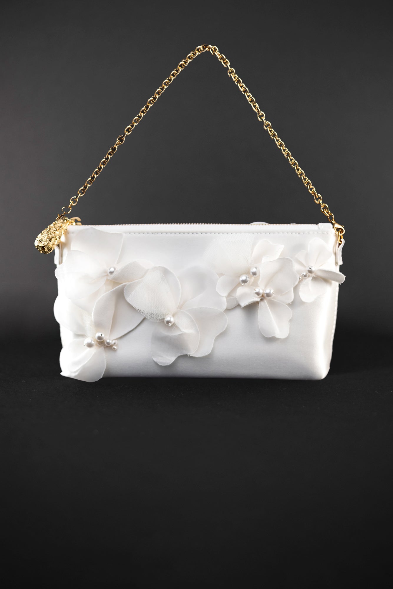 A small white Hayden clutch purse from The Bella Rosa Collection, featuring delicate organza floral design and a gold chain strap, beautifully contrasted against a black background.