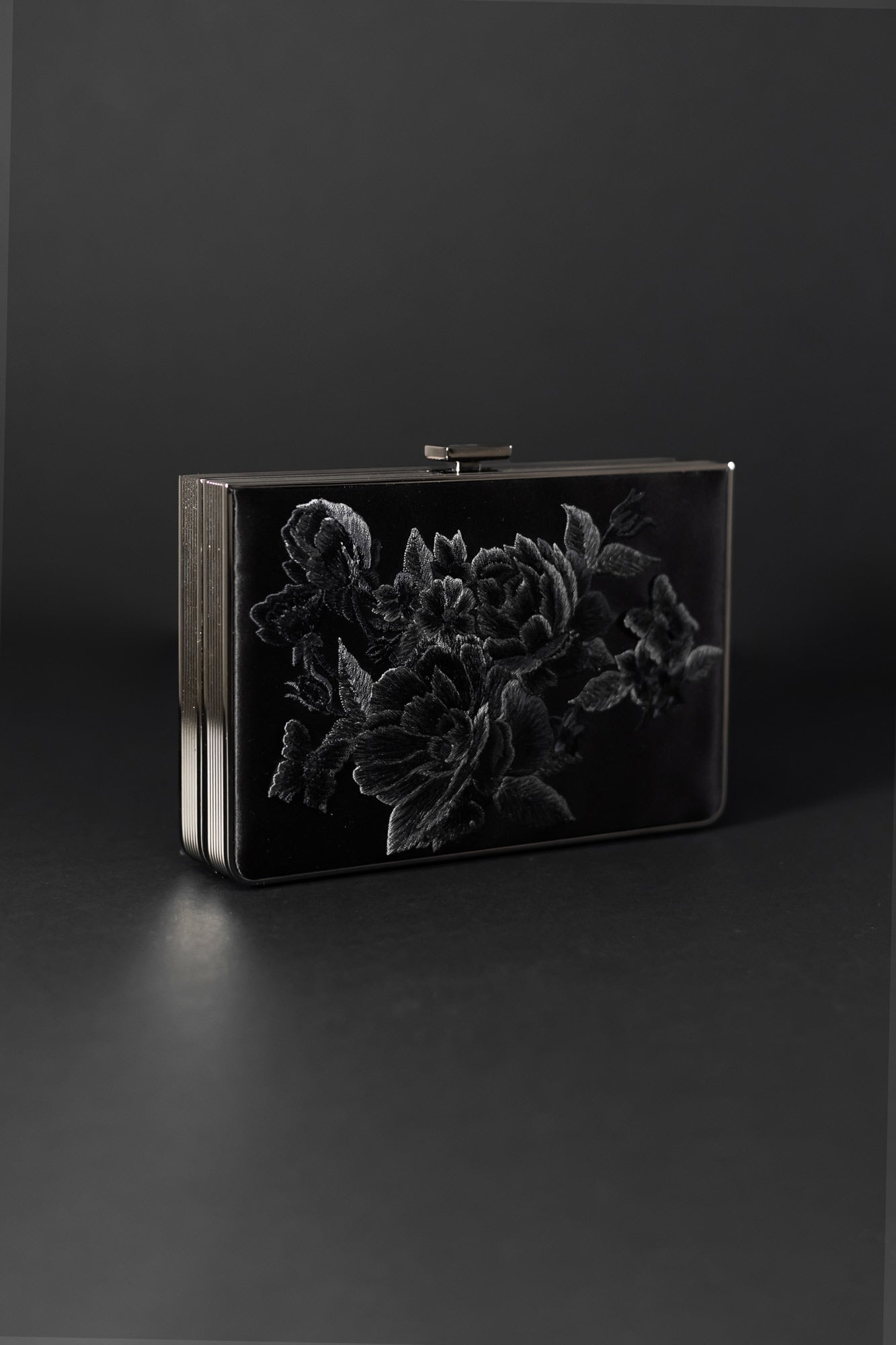 Here's the rewritten sentence:
The Venezia Clutch x MICAELA Black Satin Floral Embroidery from The Bella Rosa Collection, featuring exquisite embossed floral patterns and a refined metal clasp at the top, elegantly stands out against a dark background. Perfect for those seeking timeless elegance, this accessory adds sophistication to any outfit. Don’t miss the sample sale to own this stunning piece!
