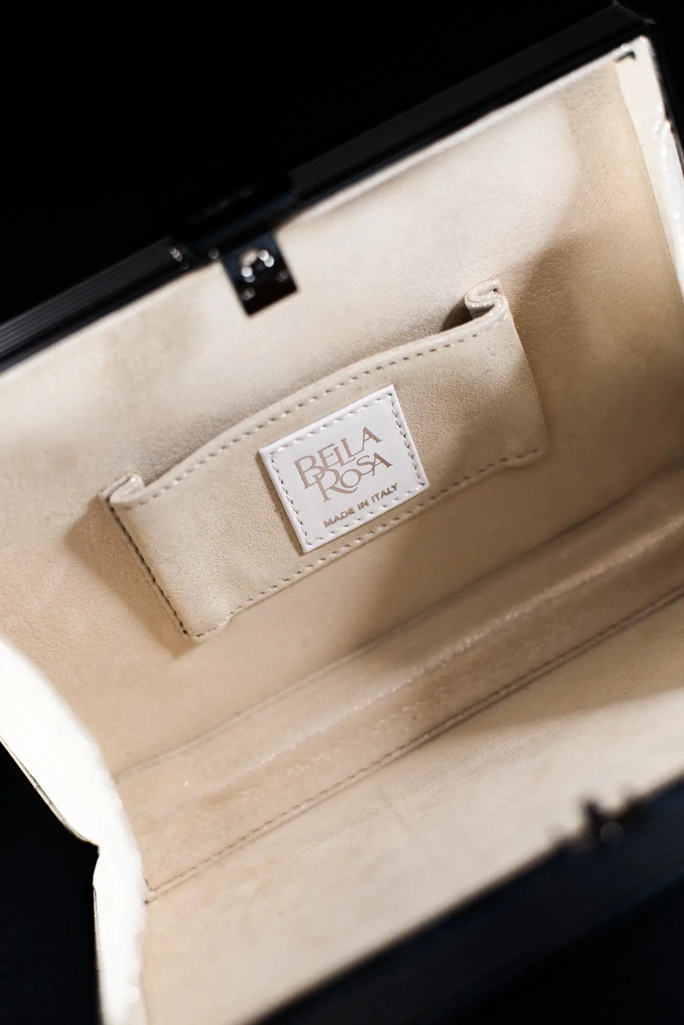 Close-up of the inside of a black satin clutch with a visible label reading "THE BELLA ROSA COLLECTION, MADE IN ITALY." Hints of floral embroidery add an elegant touch to this exquisite piece.