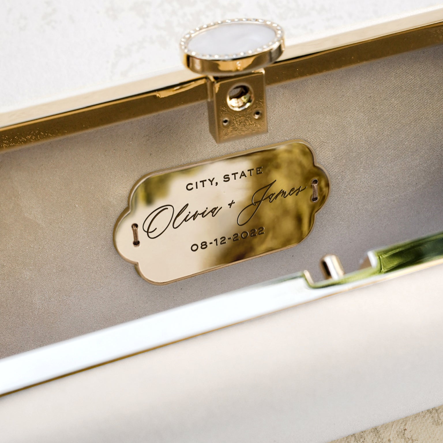 A personalized nameplate with the names "oliver + james" and the date "08-12-2022" attached to a Bella Rosa Collection Bella Fiori Clutch Ivory Clutch Petite, possibly part of a wedding item.
