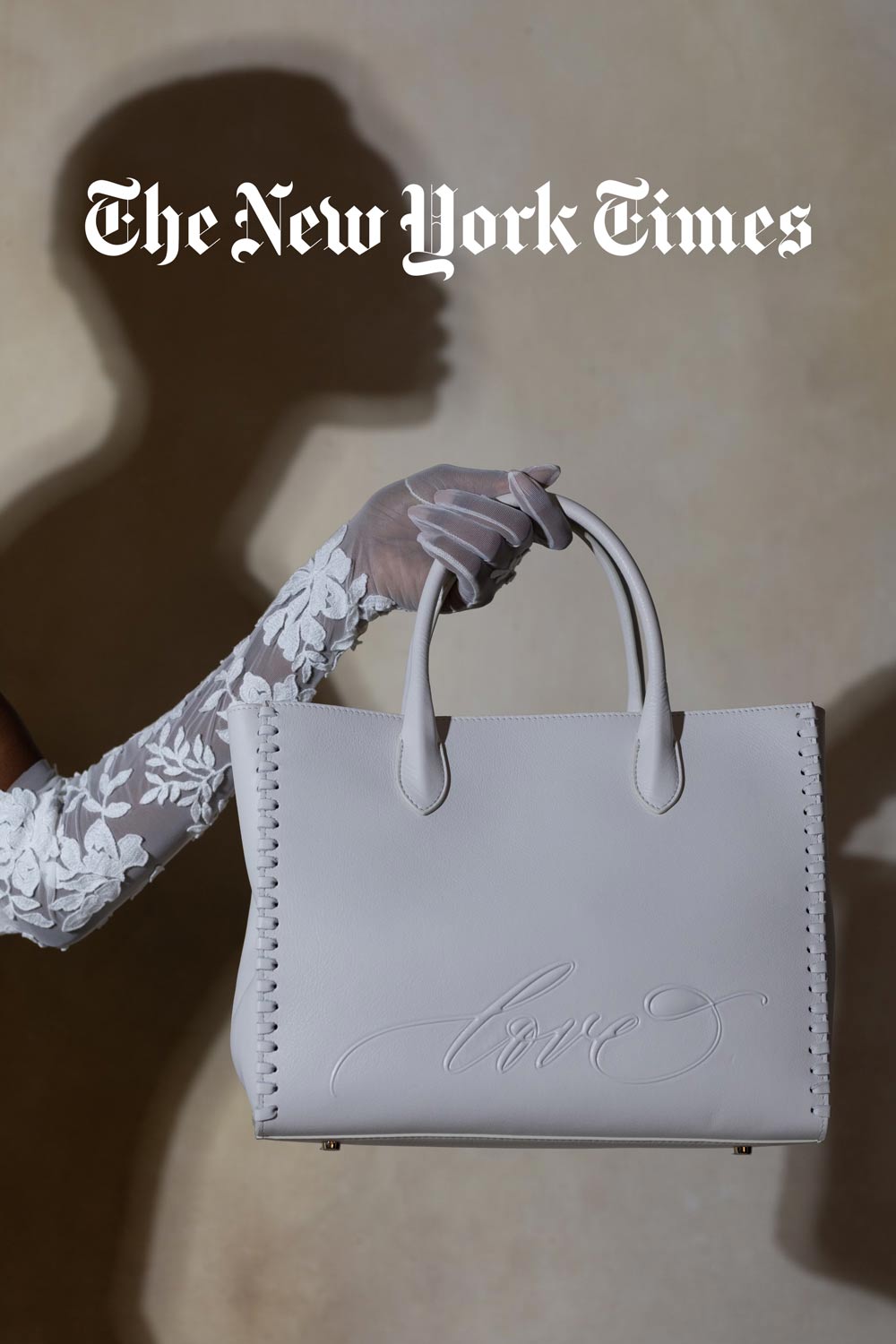 A person in a lace glove holds a light-colored handbag with "love" embossed on it, under "The New York Times" logo on a neutral background.