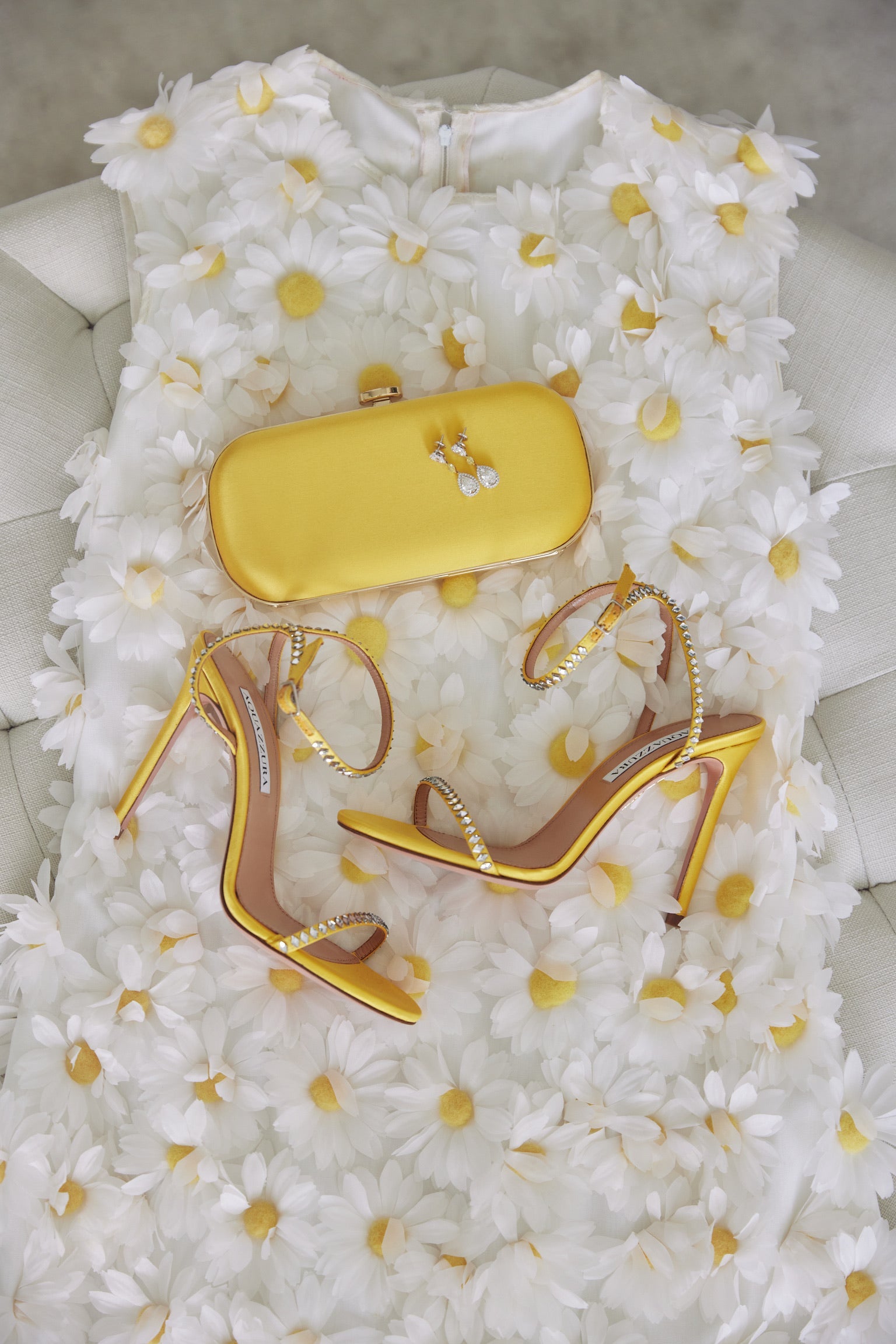 A dress, heels, and a Bella Rosa Collection Limoncello Yellow Petite Clutch adorned with rhinestones, displayed on a bed of white flowers.