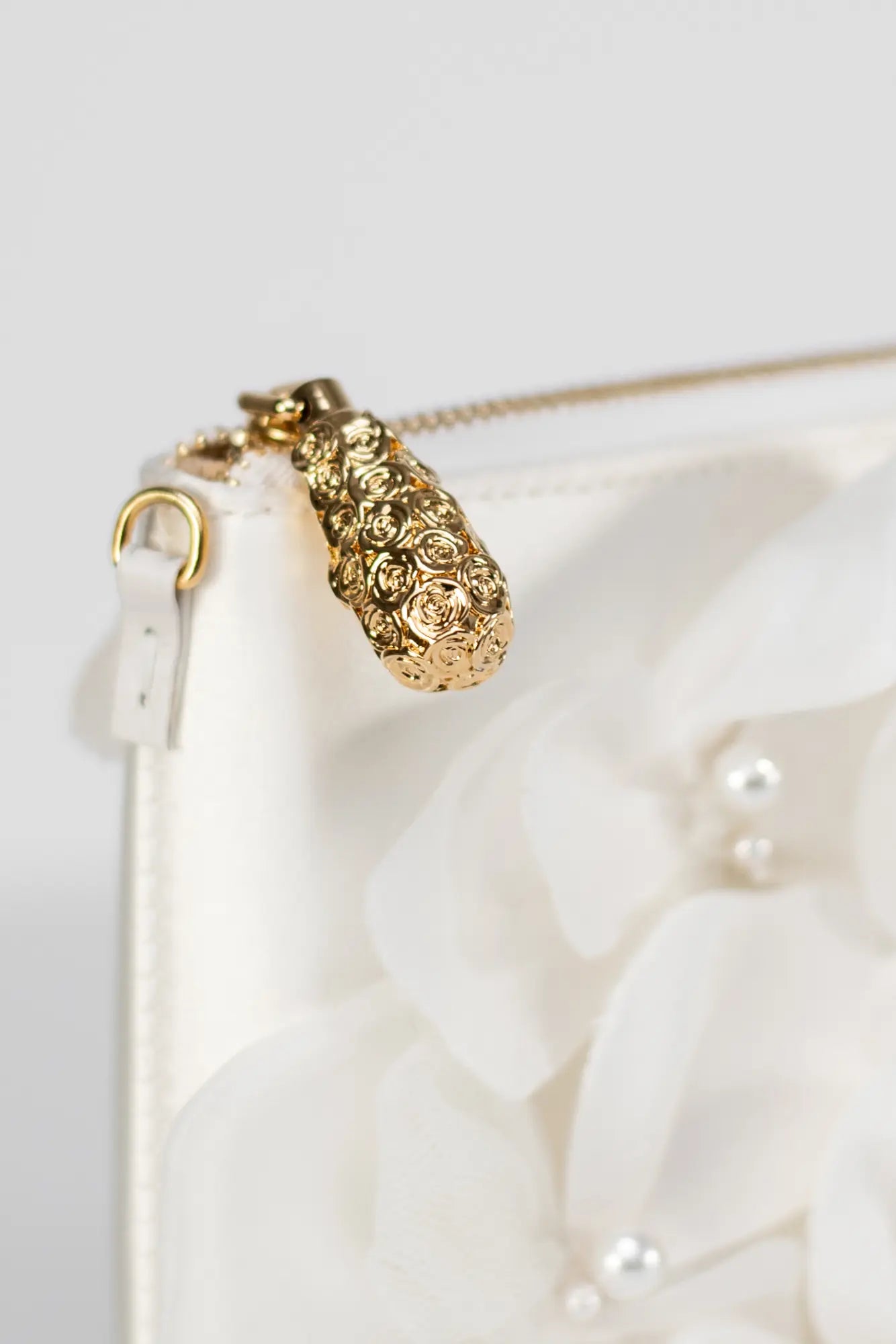 Close-up of The Bella Rosa Collection's Hayden Clutch Purse from the Sample Sale, made of exquisite Ivory Duchess Satin with a gold floral zipper pull and delicate organza flower embellishments featuring small pearls, showcasing exceptional Italian craftsmanship.