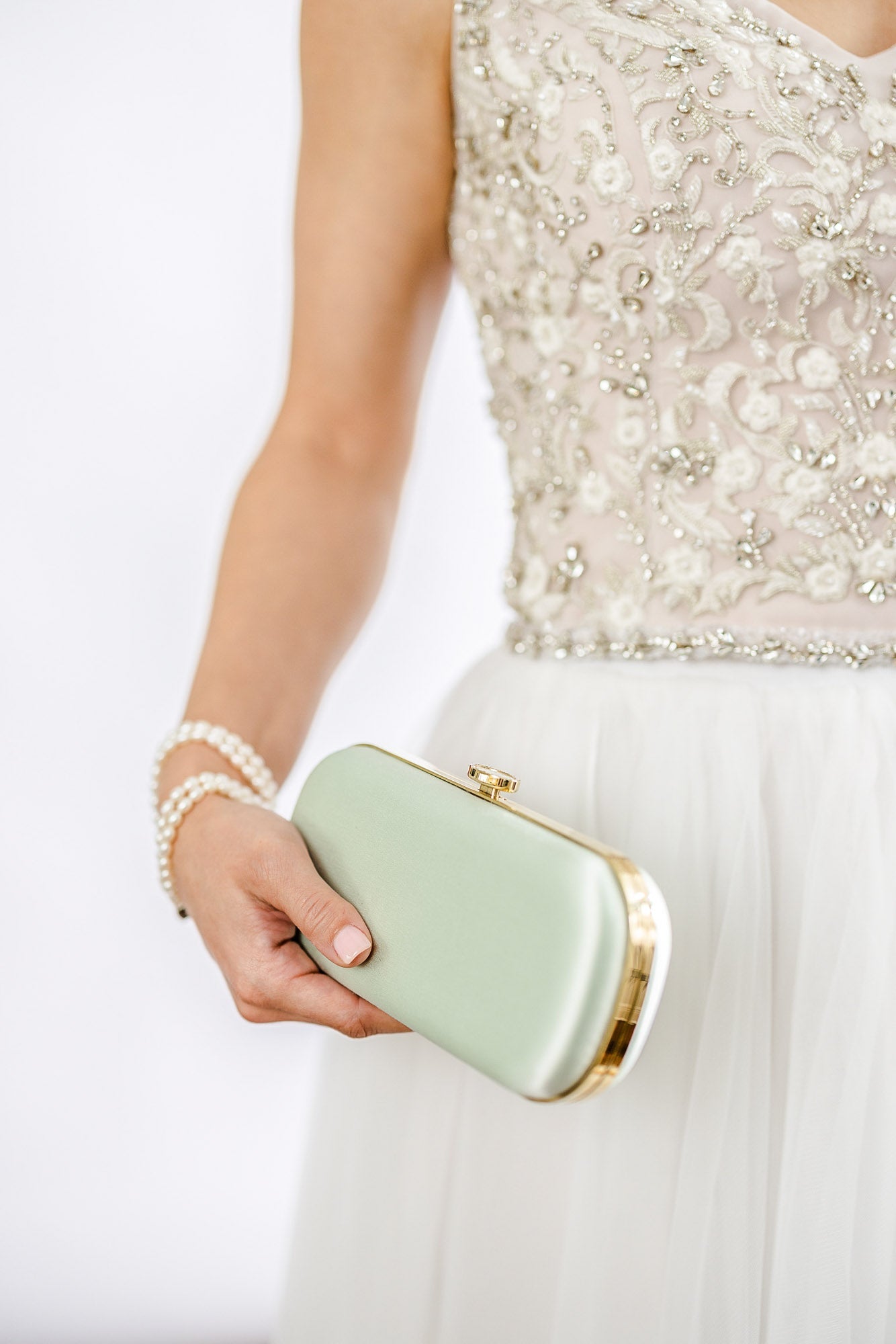 Woman in an embellished dress holding a Bella Rosa Collection Sage Green Satin Petite Clutch.