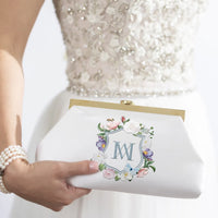 A woman in a white dress holding a Rosa Clutch - Ivory Floral Embroidery from The Bella Rosa Collection.