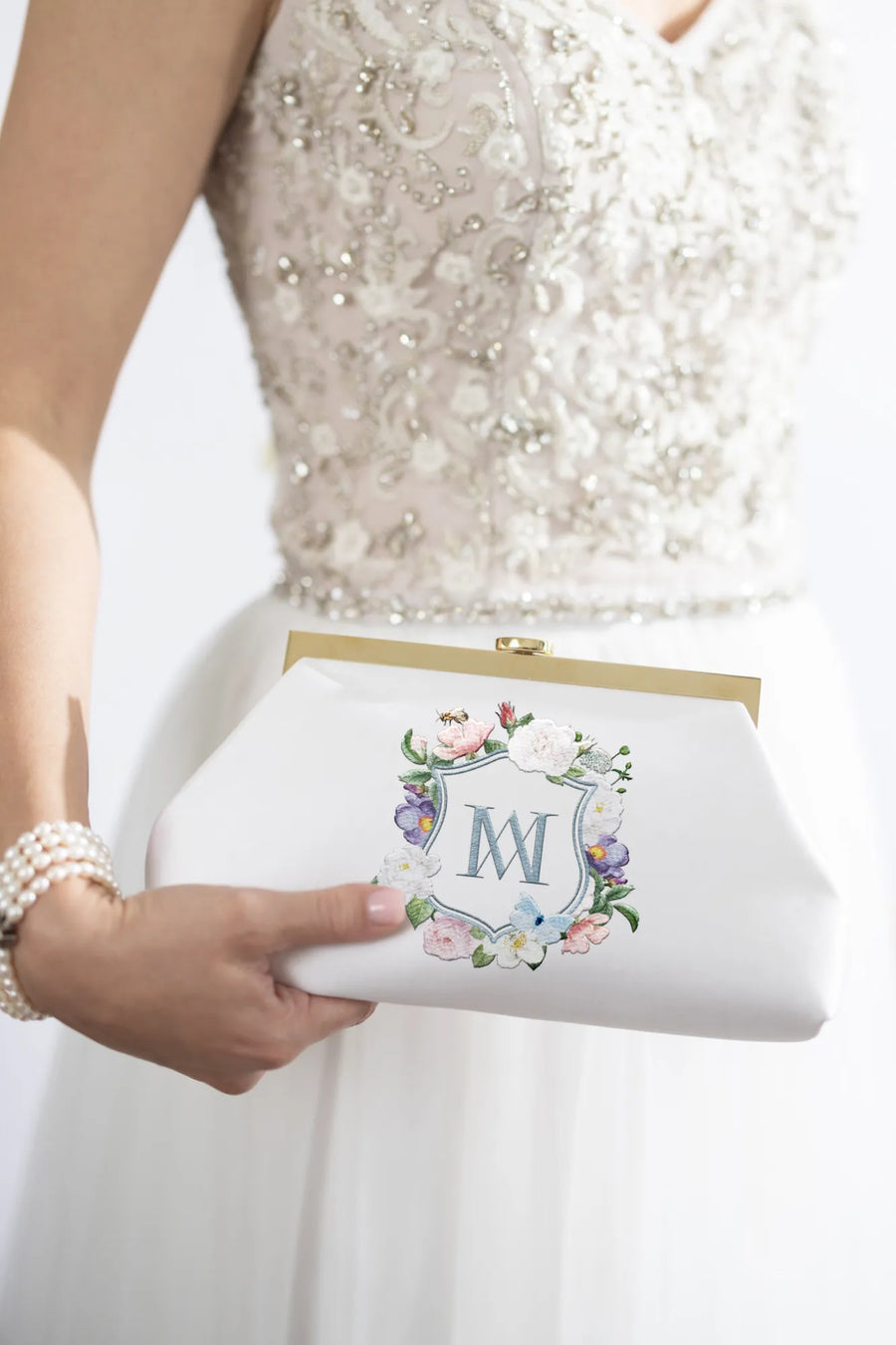 A woman in a white dress holding a Rosa Clutch - Ivory Floral Embroidery from The Bella Rosa Collection.
