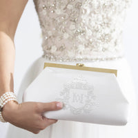 A bride wearing a wedding dress, holding a white vintage bridal, clutch with custom monogram white embroidery.