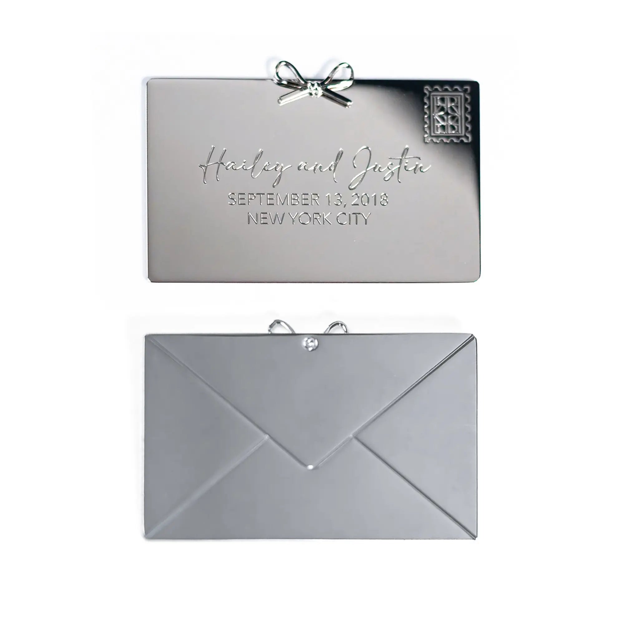 Silver wedding invitation with a bow, displaying names and date, alongside its envelope, featuring The Bella Rosa Collection Personalized Plaque Sentiment Engraving.