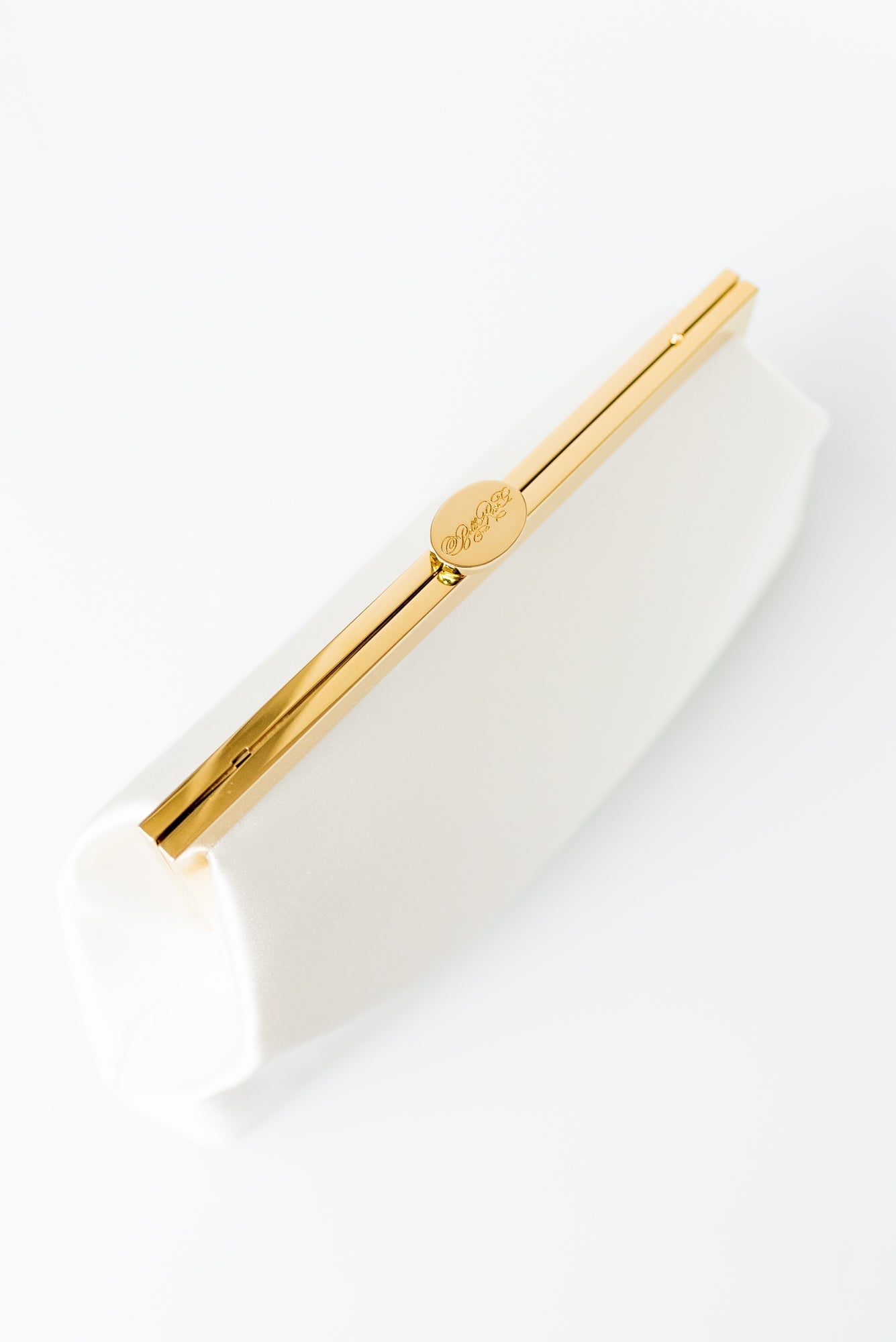 A gold-colored pen placed diagonally across a white The Bella Rosa Collection Rosa Clutch Monogram Embroidery with floral embroidery.