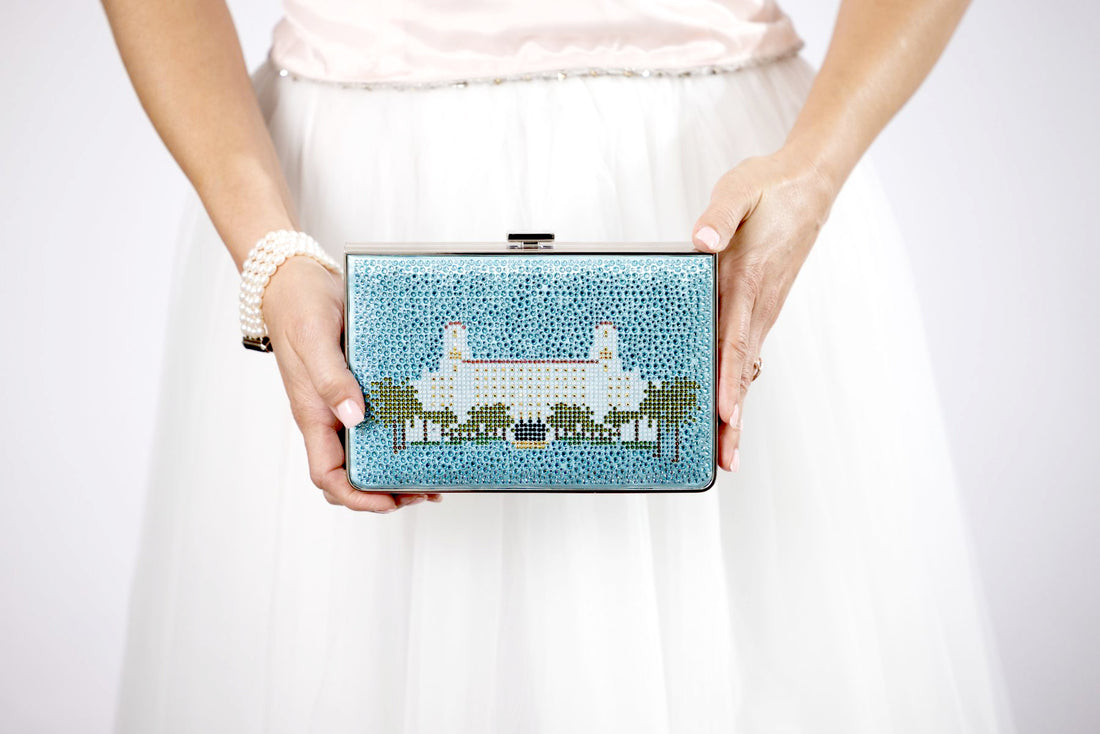 A woman from Palm Beach is holding a Breakers Crystal Rhinestone Clutch from The Bella Rosa Collection, featuring a stylish blue building design.