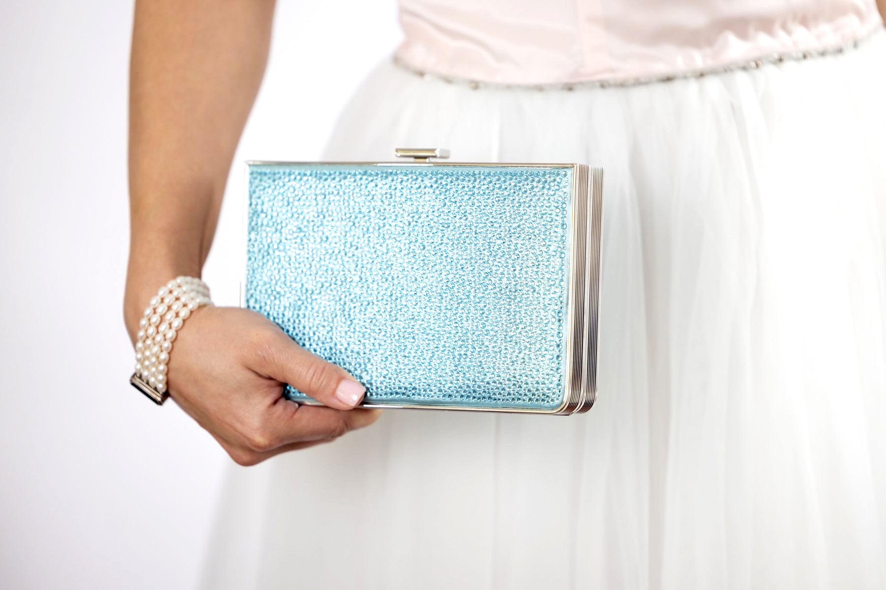 In Palm Beach, Florida, a woman wearing a white dress elegantly holds a Breakers Crystal Rhinestone Clutch from The Bella Rosa Collection.