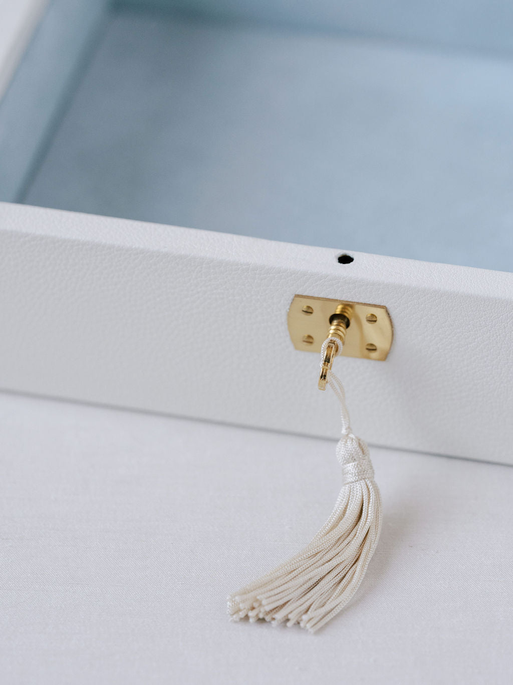 Close up image of the white Italian leather wedding keepsake box. Shown is the gold accented key with tassel inserted into the key hold. Box is open with blue suede interior and can hold all wedding day mementos.