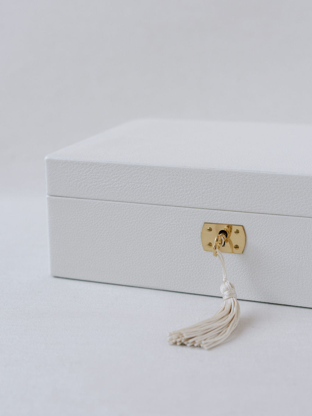 White Italian leather wedding day keepsake box shown closed with gold key with white tassel inserted into a key lock. 