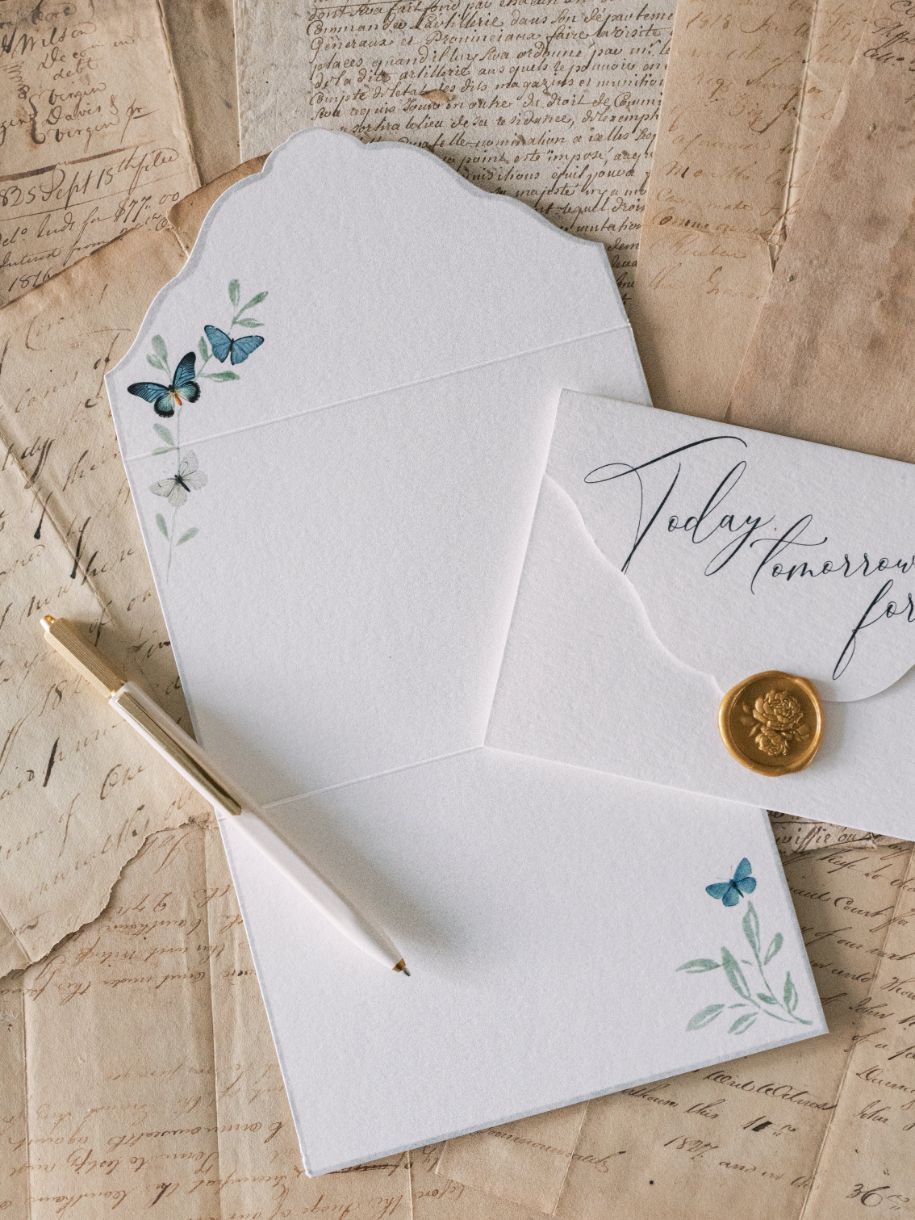 A watercolor floral motif letter, envelope, and pen on top of a Wedding Day Love Note Box Stationery Set from The Bella Rosa Collection.