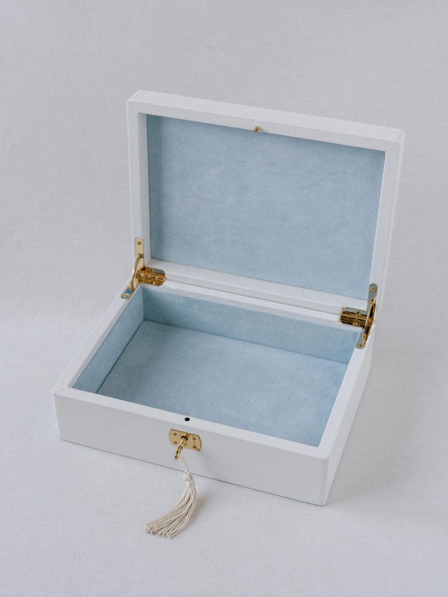 White Italian leather wedding keepsake box. Shown is the gold accented key with tassel inserted into the key hold. Box is open with blue suede interior and can hold all wedding day mementos.