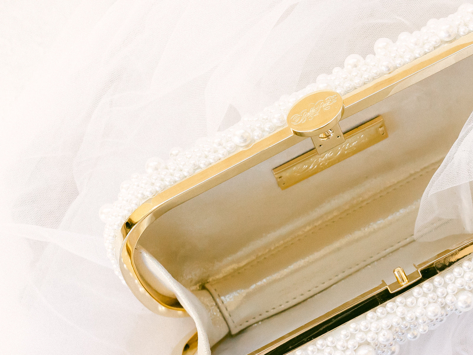 An elegant True Love Pearl Petite Bella Clutch from The Bella Rosa Collection, adorned with pearls, partially obscured by a translucent white fabric.