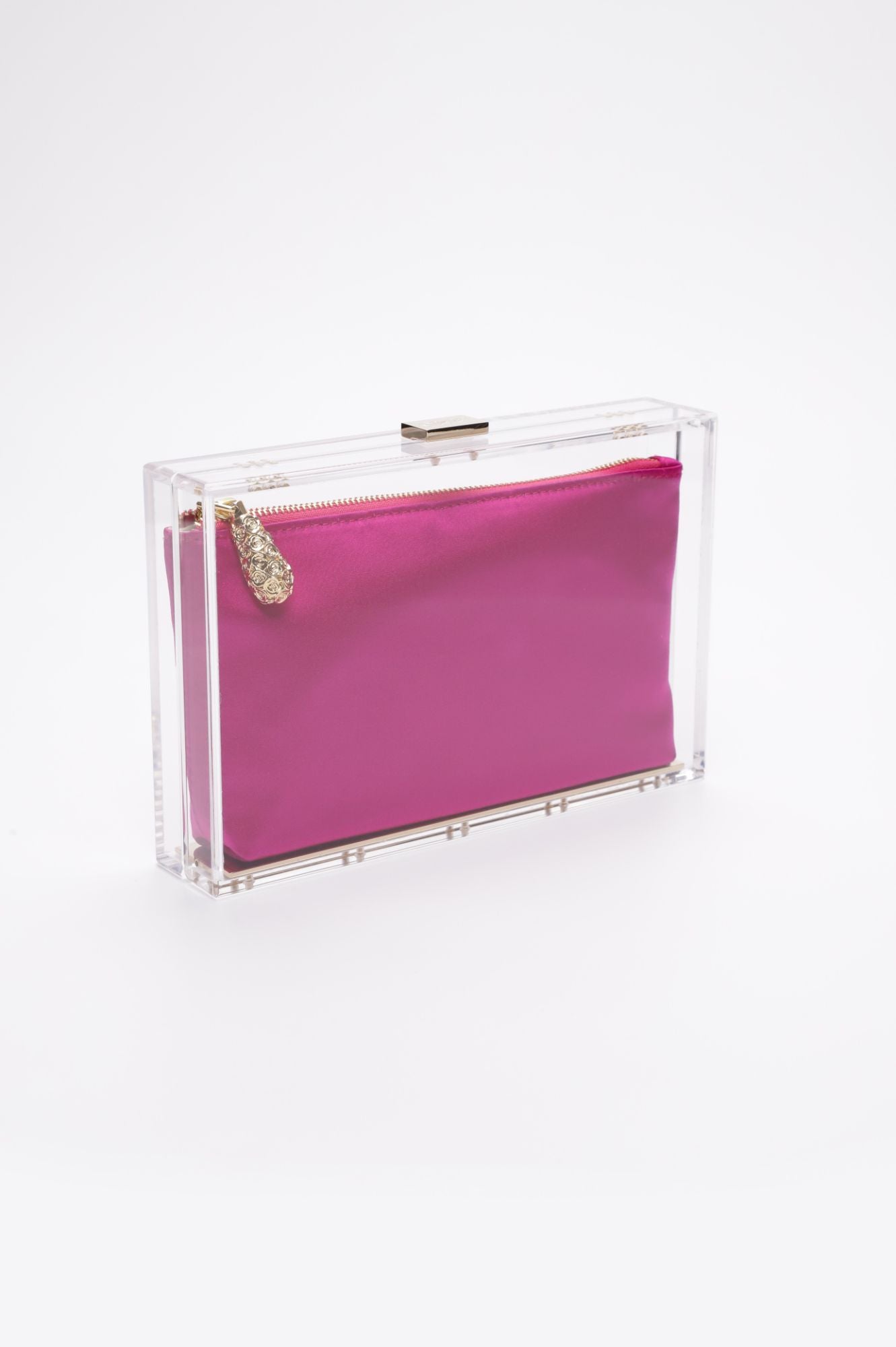 A hot pink Mia Clutch bag, encased in a clear rectangular case with a gold zipper and adorned with a decorative gold charm, is displayed against a plain white background. This stylish piece is from The Bella Rosa Collection&#39;s exclusive sample sale.