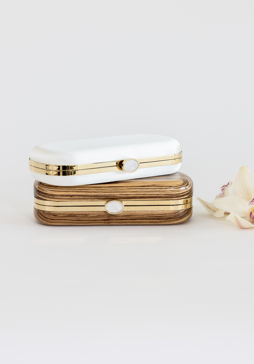 Bella Clutch with a gold hardware frame in a solid African Zebra Wood Body stacked below a Bella Clutch in Ivory.