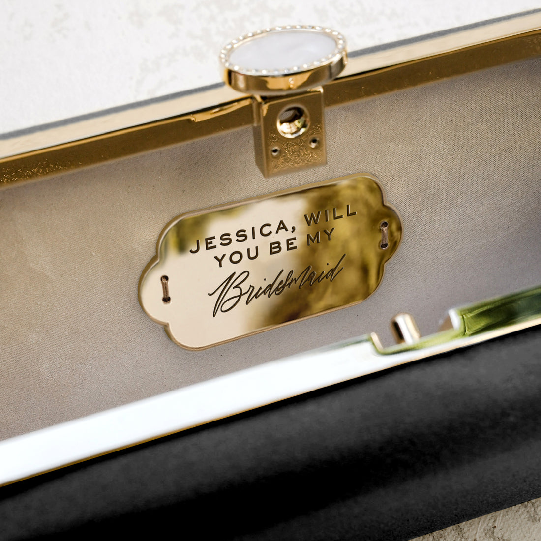 A customized Bridesmaid Proposal Box with Engraved Bella 'Be My Bridesmaid' Clutch Bag Gift in black and gold, with the words "Jessica, will you be my bridesmaid?" by The Bella Rosa Collection.