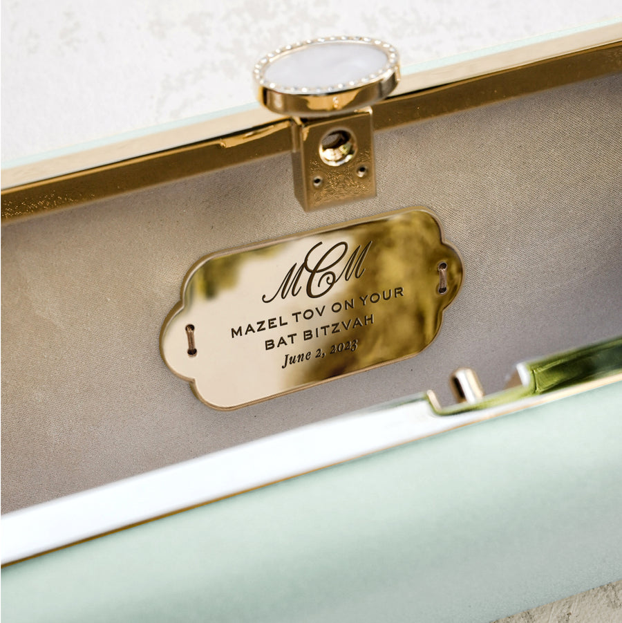 The Bat Mitzvah Personalized Bella Clutch Petite from The Bella Rosa Collection, a personalized gift perfect for a Bat Mitzvah, features a beautiful mint green color and is adorned with a luxurious gold tag.