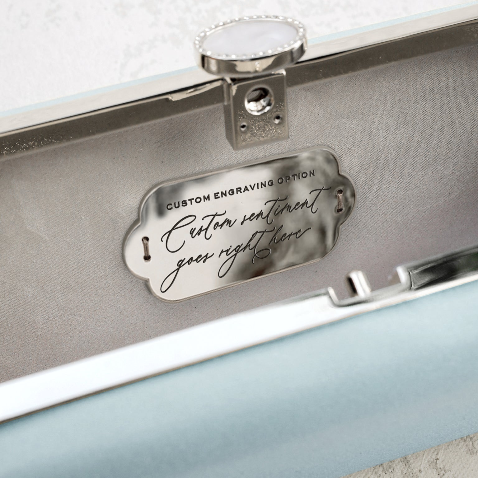 A Bella Clutch Cinderella Blue Petite from The Bella Rosa Collection with custom wedding accessory engraving inside a case displaying an example message.