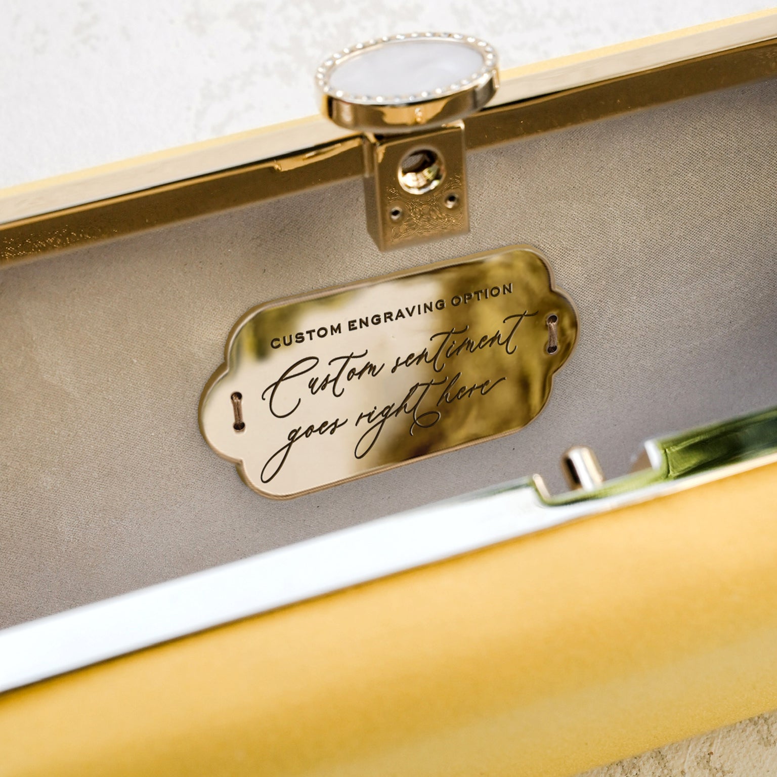 Gold engraved plate inside a jewelry box, offering a custom engraving option alongside The Bella Rosa Collection&#39;s Bella Clutch Limoncello Yellow Petite, a luxury bridal handbag.