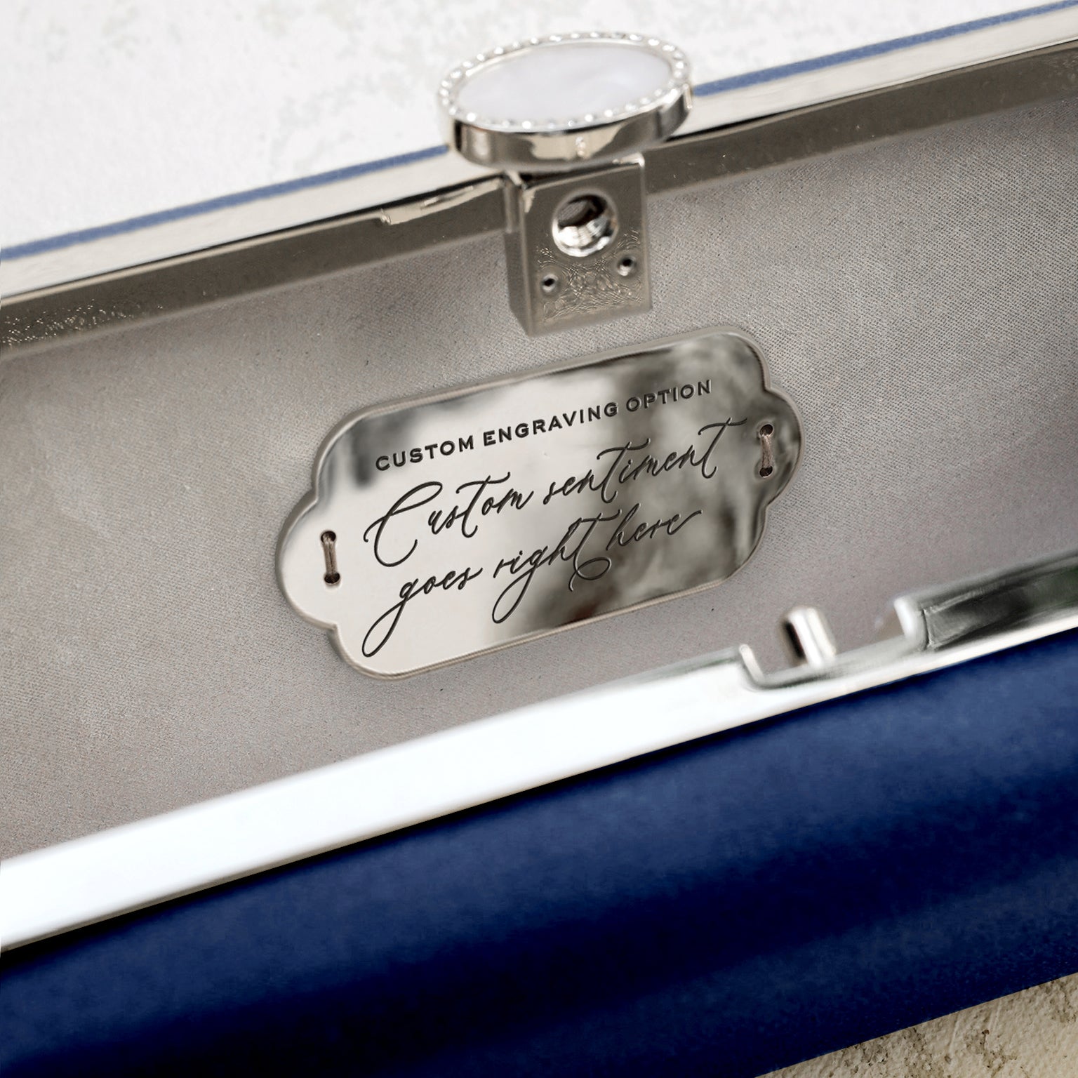 A briefcase interior showing a custom engraving plate with promotional text for the Navy Blue Petite Bella Clutch evening clutch from The Bella Rosa Collection.