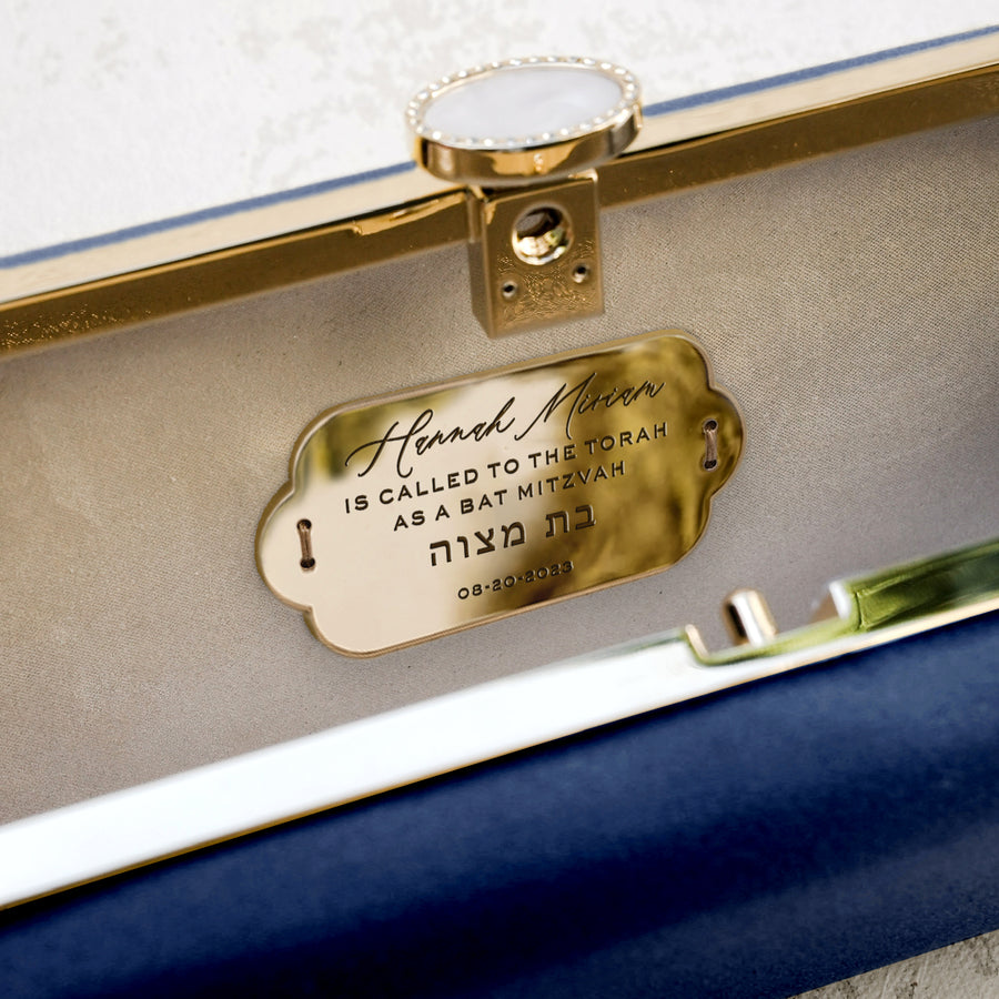 The Bat Mitzvah Personalized Bella Clutch Petite, a gift perfect for a Bat Mitzvah celebration, is adorned with a gold tag. (Brand: The Bella Rosa Collection)
