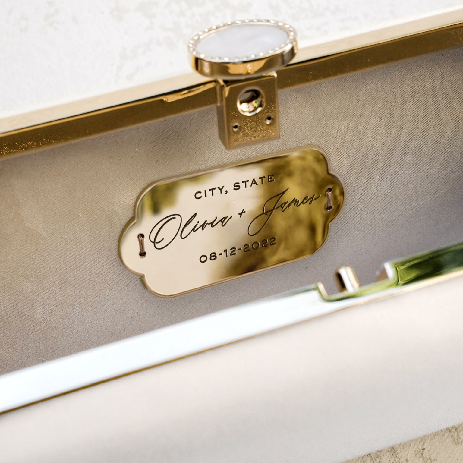 A personalized nameplate with the names &quot;oliver + james&quot; and the date &quot;08-12-2022&quot; attached to a Bella Rosa Collection Bella Fiori Clutch Ivory Clutch Petite, possibly part of a wedding item.