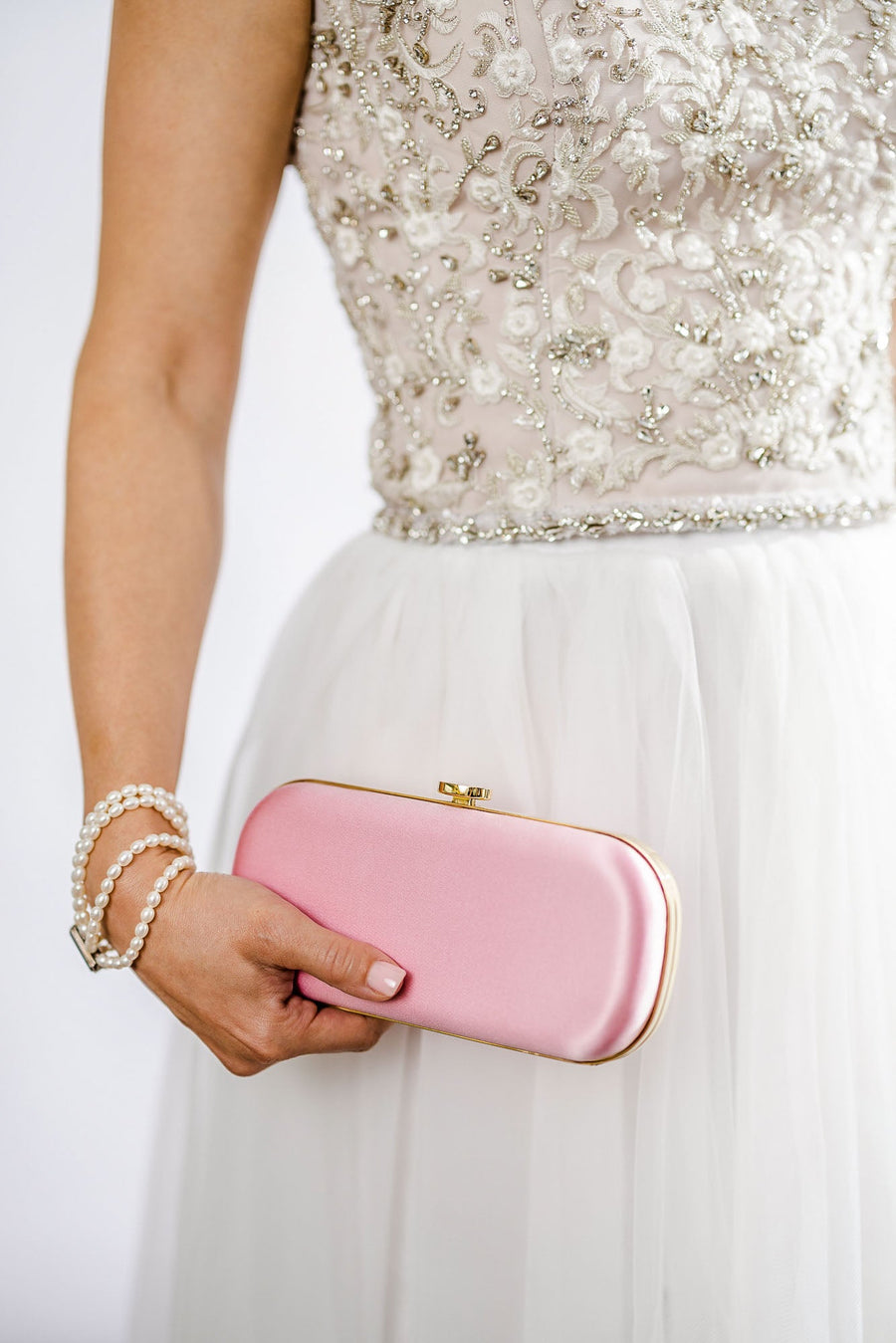 A woman in a white dress holding a Pink Satin Bella Clutch from The Bella Rosa Collection, handcrafted in Italy.