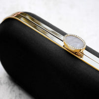 Close up view of Black Satin Bella Clutch with gold hardware and stimulated pearl clasp.