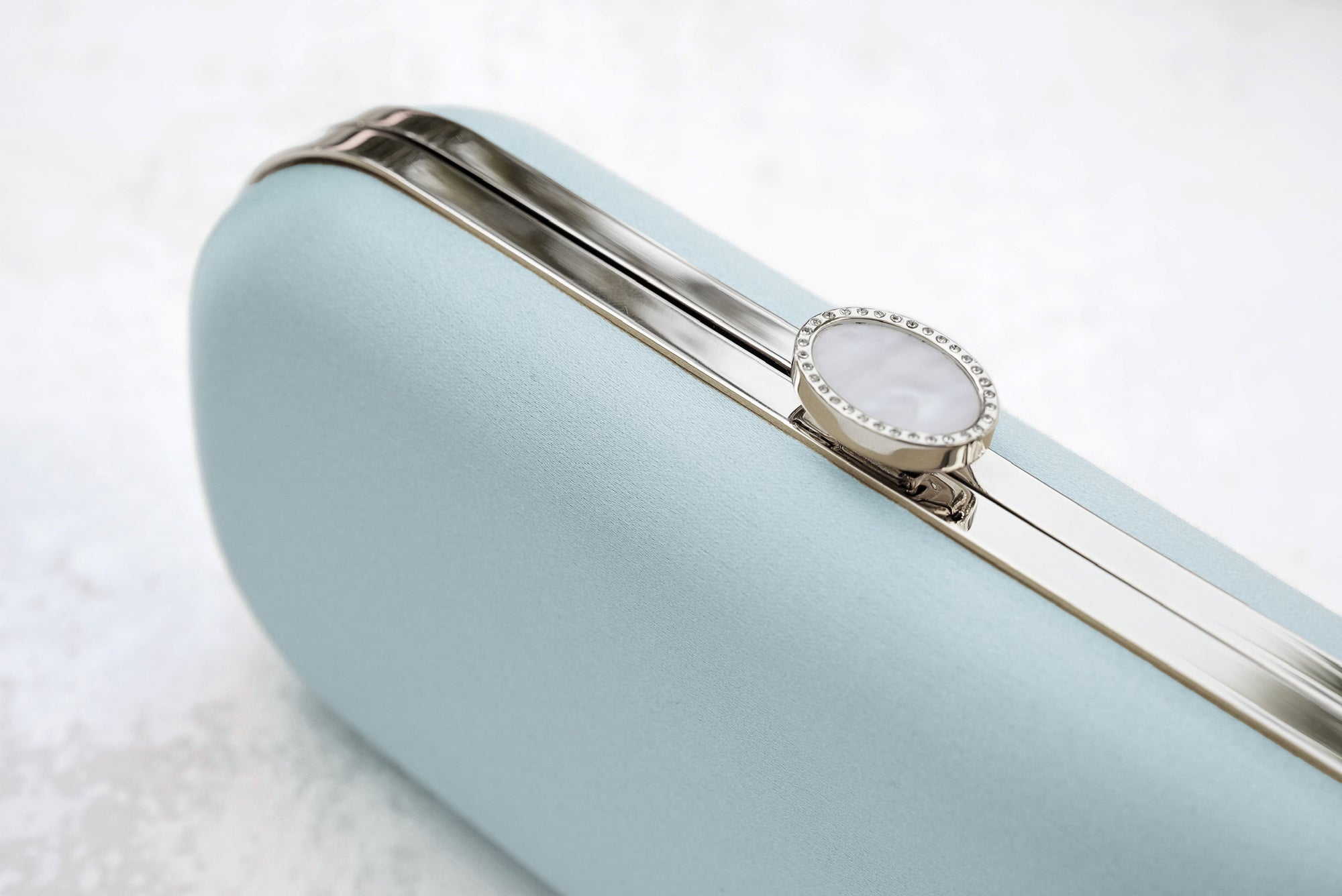 Elegant wristwatch with a white face and silver detailing resting on a pale blue The Bella Rosa Collection Cinderella Blue Petite Bella Clutch.